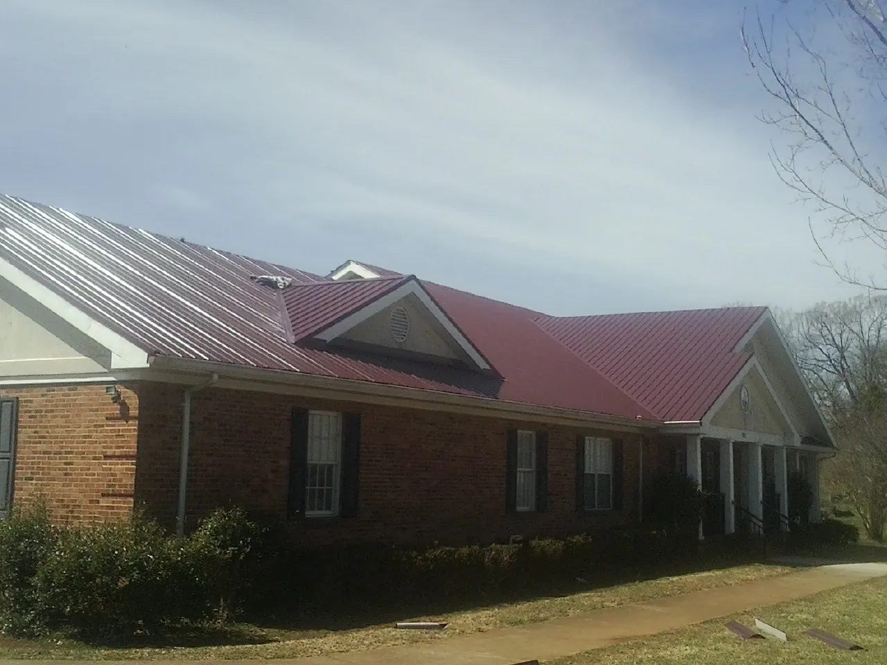 Red metal roof with gabled entries on a long brick building, from a Hail Damage Roof Repair job in Worthing